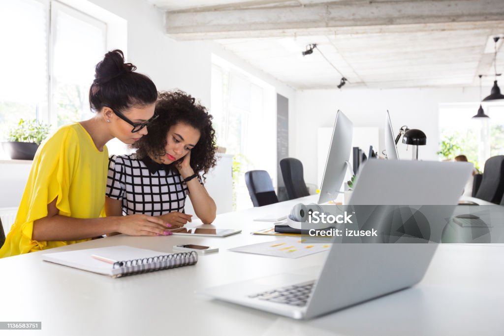 Creative women working together Shot of two creative women working together on digital tablet at office 20-24 Years Stock Photo