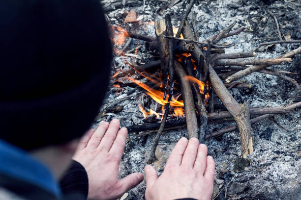 istock man warms his hands near a small fire in the forest 1136585343