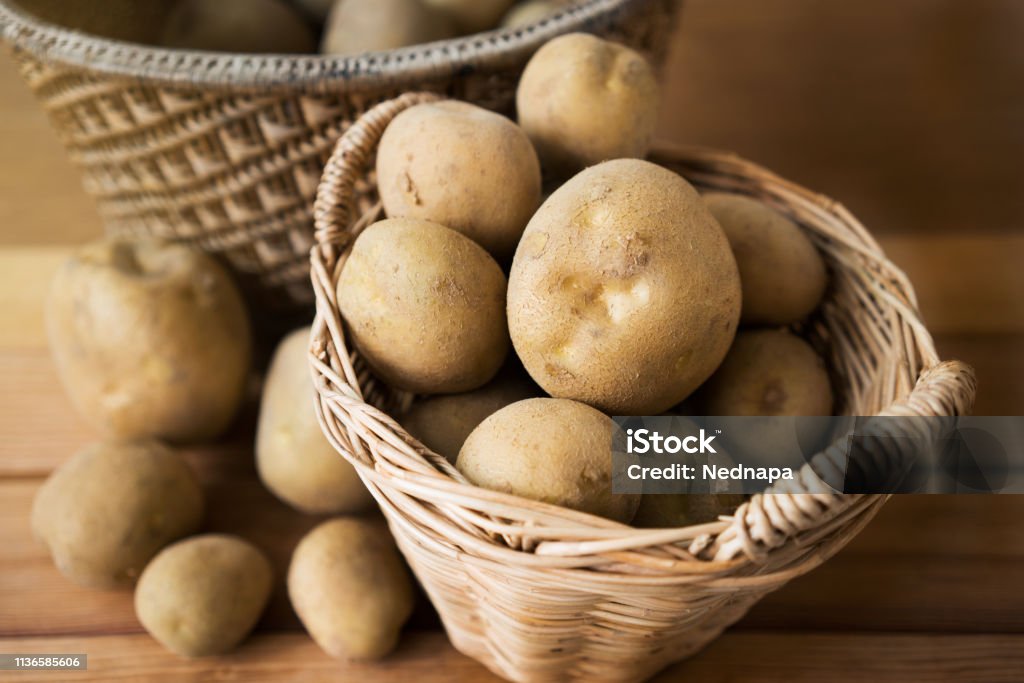 potatoes in basket. potatoes in a wicker basket on wood. Raw Potato Stock Photo