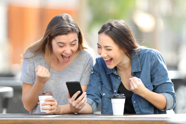 Excited friends celebrating online news on phone Excited friends celebrating online news on phone Best Student Apps stock pictures, royalty-free photos & images