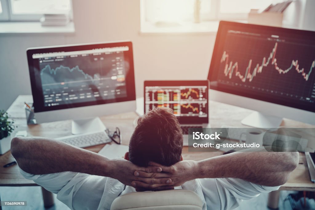 Time to relax. Top rear view of young businessman in formalwear holding hands behind head while sitting in the office Investment Stock Photo