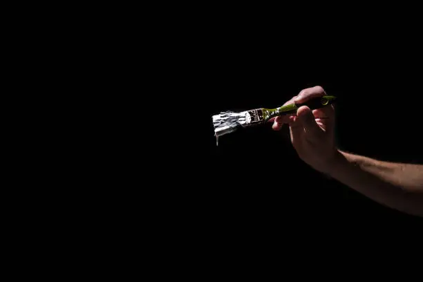 Photo of male hand holding a brush with white paint on a black background. Man in industrial concept.