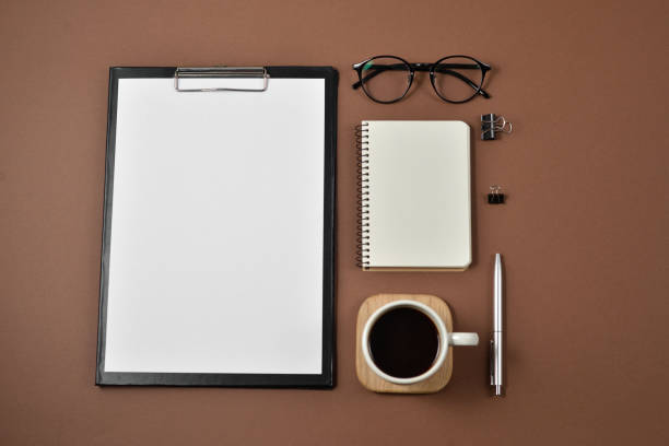 istock Mock up workspace with blank clip board, office supplies, pen, coffee cup, notepad and eyeglasses on brown background. Flat lay, top view, copy space 1136596877