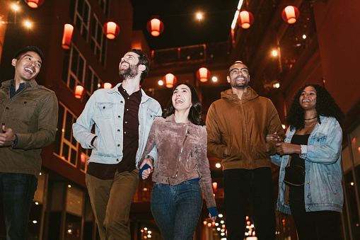 A diverse group of multiethnic friends walk the streets of Chinatown in L.A. California on a warm evening, exploring the cities night life.  Bright traditional lanterns illuminate the scene.