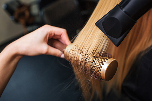 Cliente femenino en salón de belleza. Primer plano de los peluqueros secado a mano cabello rubio con secador de pelo y cepillo redondo, haciendo nuevo peinado photo