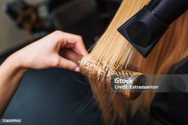 Female Client In Beauty Salon Closeup Of Hairdressers Hand Drying Blond Hair With Hair Dryer And Round Brush Doing New Hairstyle Stock Photo - Download Image Now