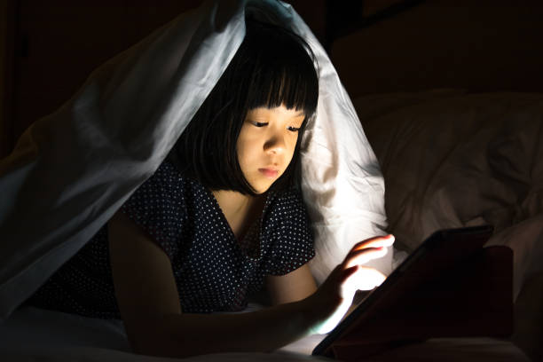 concetto di problema tablet con bambini. asia piccola bambina bambina che si intrufola usando il pc del computer smartphone di notte in camera da letto. adorabile ragazza delle elementari che guarda il film a letto. - homework teenager education mobile phone foto e immagini stock