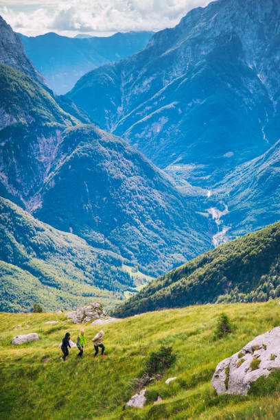 Hikers climbing uphill on steep rocky mountain trail. Summer adventures and exploration on the Alps. Beautiful valley in the background.