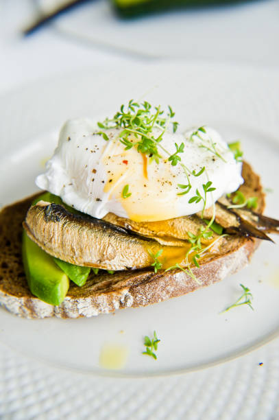 istock Toast of black bread with avocado, poached egg and sprats. White background, side view, close-up. 1136602054