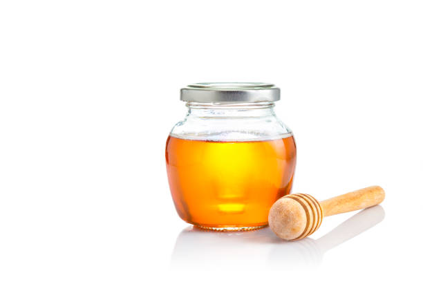 honey in closed lid glass jar with wooden honey dipper at its side, all on white background with copy space - japanese maple imagens e fotografias de stock