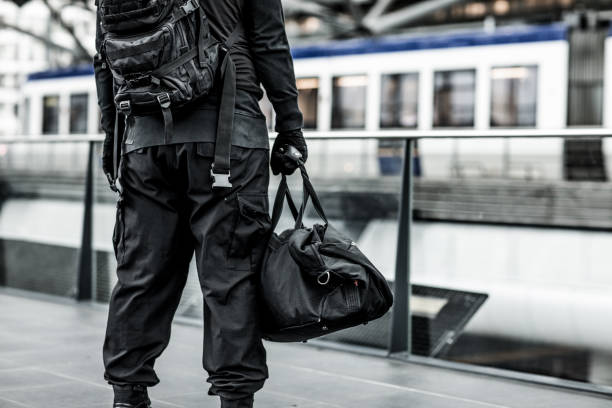 dark hooded terrorist figure at public transport hub - terrorism imagens e fotografias de stock