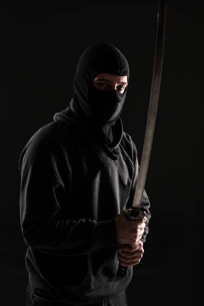 istock Man with balaclava and katana sword on black background 1136608650