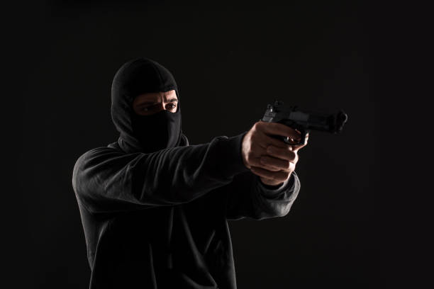 istock The robber in a mask with a gun pointed to the side on a black background 1136608655