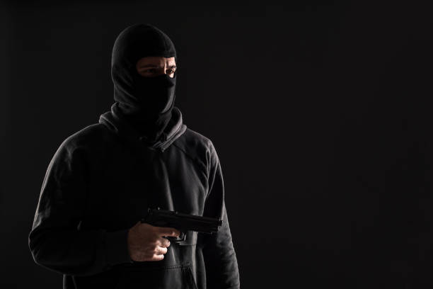 istock The robber in a mask with a gun pointed to the side on a black background 1136608664