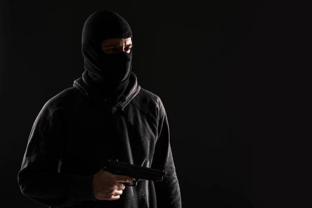 istock The robber in a mask with a gun pointed to the side on a black background 1136608665