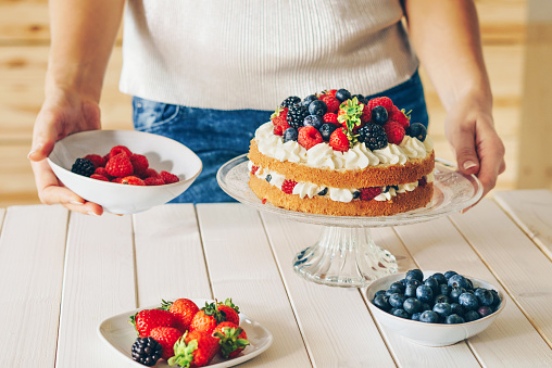 Woman decorating a sponge layer cake with fresh berries