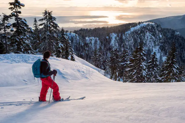 Adventurous man is backcountry skiing up Mount Seymour during a sunny winter sunset. Taken in North Vancouver, BC, Canada.