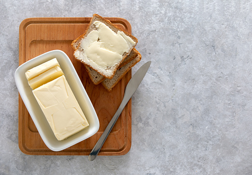 Butter or spread is in white butter-dish standing on a kitchen table and sandwich served on board ready to eat, view from above, space for a text