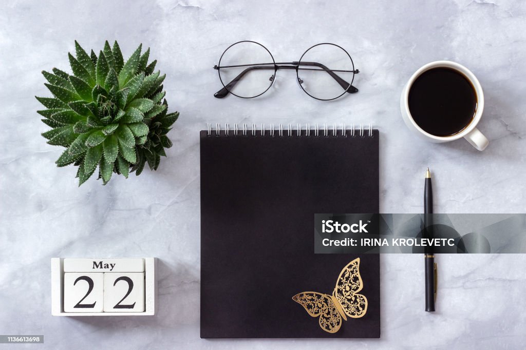 Office or home table desk. Wooden cubes calendar May 22. Black notepad, cup of coffee, succulent, glasses on marble background Concept stylish workplace Flat lay Top view Anniversary Stock Photo