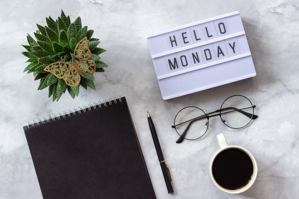 Office or home table desk. Lightbox text hello monday Black notepad, cup of coffee, succulent, glasses on marble background Concept stylish workplace Flat lay Top view