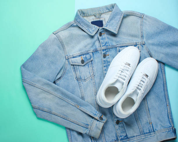 istock Flat lay style white hipster sneakers with a denim jacket on a pastel blue background. Retro culture, top view 1136614788
