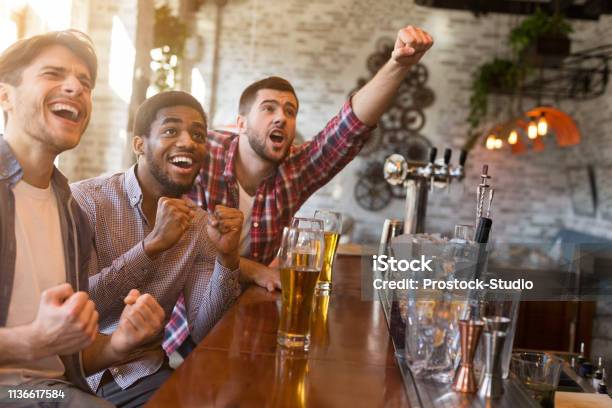 Photo libre de droit de Hommes Encourageant Pour Léquipe De Football Dans Le Bar De Sport banque d'images et plus d'images libres de droit de Bar