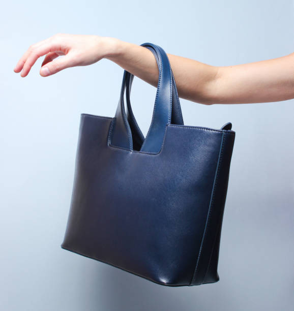 istock Leather handbag hangs on female hand on gray background 1136618876