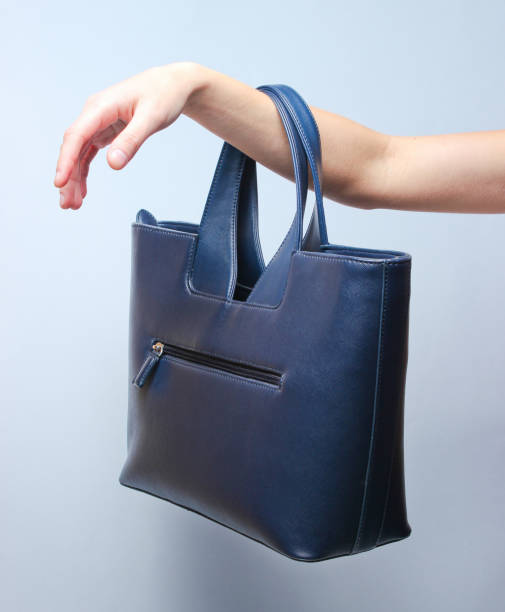 istock Leather handbag hangs on female hand on gray background 1136618877