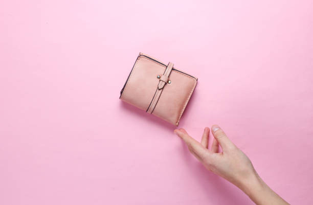 Minimalism trend. Female hand takes pink leather wallet on pink pastel background. Top view stock photo