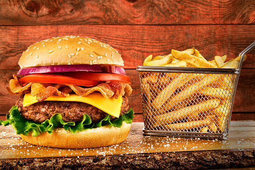 Cheeseburger with bacon and a basket of french fries. Wooden plank in background. Copy space for your text.