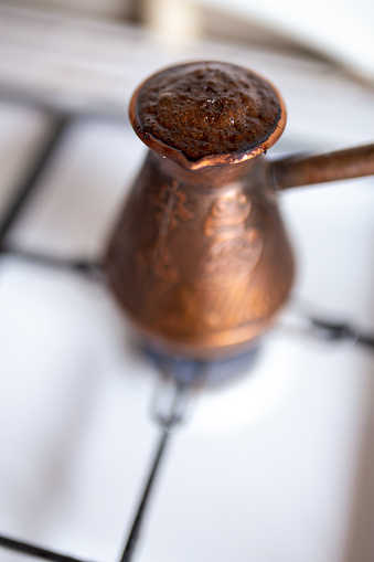 Coffee brewed in a copper cezve on a gas stove in cozy typical kitchen in the morning. Preparing delicious coffee in cezve - very soft blurry bokeh