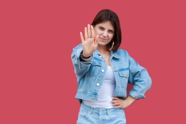 retrato de advertencia hermosa mujer joven morena con maquillaje en denim estilo casual de pie con la mano en la cintura y mirando a la cámara con las manos de stop sign. - coat concepts danger anger fotografías e imágenes de stock