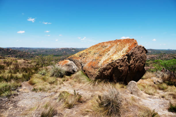 Large boulder in a field by mountain slope under blue sky