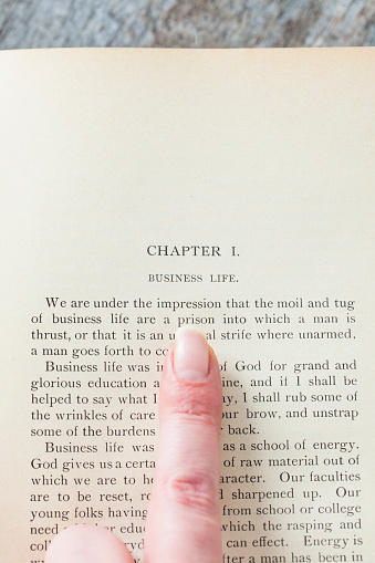 Antique hardcover book open to chapter I on Business Life with finger pointing at it.
