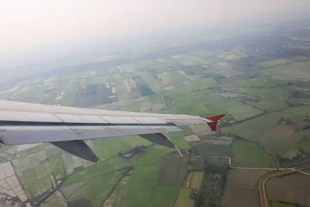 Photo of wing of airplane flying over agricultural area