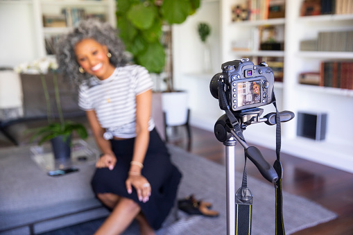 A beautiful black woman with white curly hair  sets up her camera and tripod to record a vlog for her blog