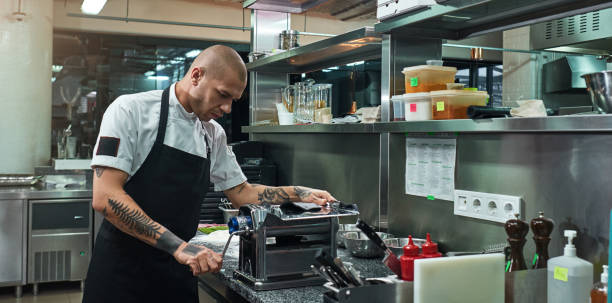 istock Concentrated at work. Serious and handsome chef with black tattoos on his hands rolling a black dough through pasta machine 1136638699