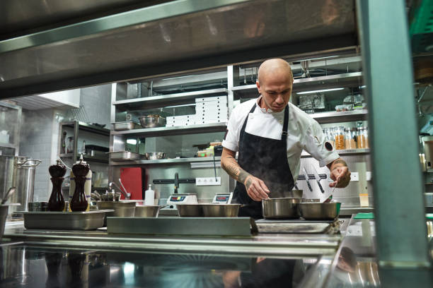 istock Restaurant chef. Concentrated young chef in black apron is cooking at his modern restaurant kitchen. 1136638813