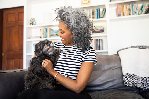 A beautiful black woman with white curly hair  cuddles on the couch with her dog