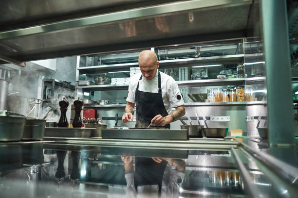 istock Professional chef. Famous young chef in black apron working at his modern restaurant kitchen 1136638929
