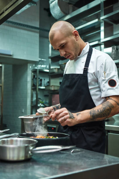istock Need more spices. Vertical photo of restaurant chef with several tattoos adding a special spice to fresh cooked pasta Carbonara. 1136638987