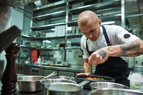 istock Delicate work. Famous confident chef with several tattoos on his arms garnishing pasta Carbonara in a restaurant kitchen. 1136639107