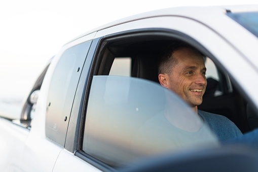 Candid portrait through car window of man smiling about to drive away from the beach in his pick up truck.