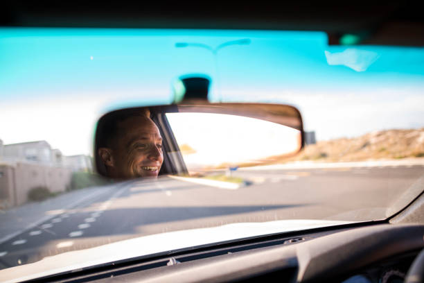istock Happy mans face in rearview mirror open road ahead 1136639262
