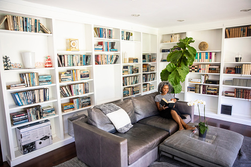 A beautiful black woman with white curly hair  reads a book on her couch in her library at home