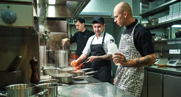 istock Dangerous work. Profesional chef teaching his two young trainees how how to flambe food safely. Cooking techniques 1136639362