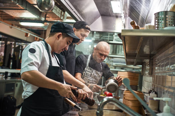istock Teamwork. Restaurant chef and his two assistants in aprons cooking a new dish in a modern kitchen. 1136639543