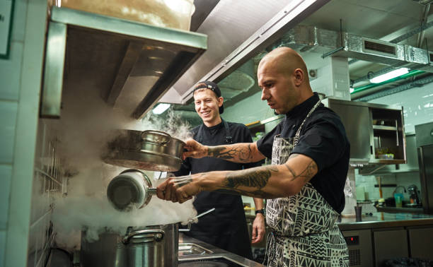 istock Culinary school. Handsome and confident chef teaching how to cook his two assistants in a restaurant kitchen 1136639570