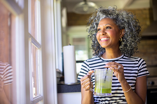 A beautiful black woman with white curly hair  drinks coffee in her kitchen