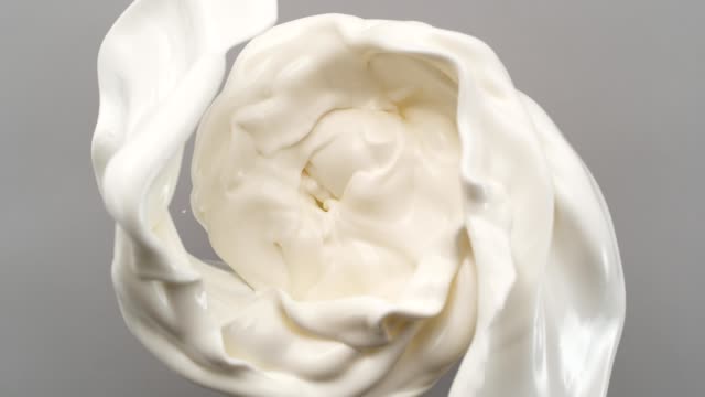 Creamy milk swirling on gray background. Super slow motion